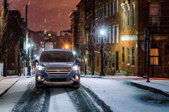 Image of a blue Ford Escape SUV driving on a snowy street.