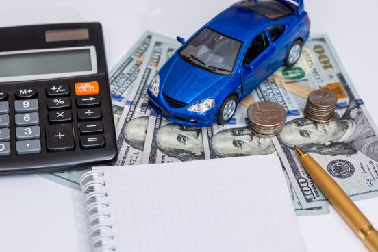 Image of a blue toy car, a calculator, and a notepad on a table with $100 bills.